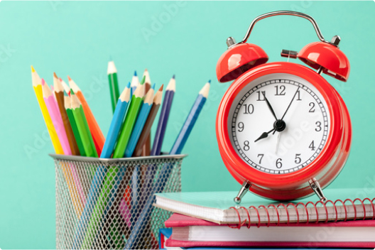 Zdjęcie przedstawiające koszyczek z kolorowymi ołówkami oraz czerwony zegar-budzik